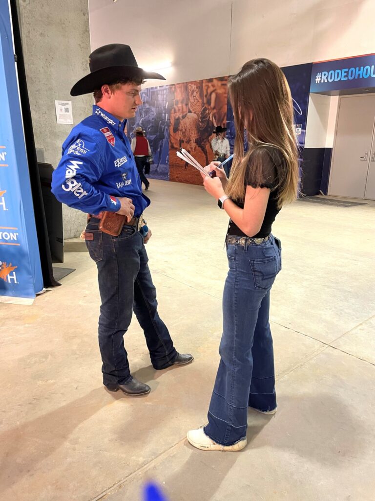 Back stage at the Houston Rodeo, a young woman who is part of the Texas A&M internships program interviews a professional cowboy.