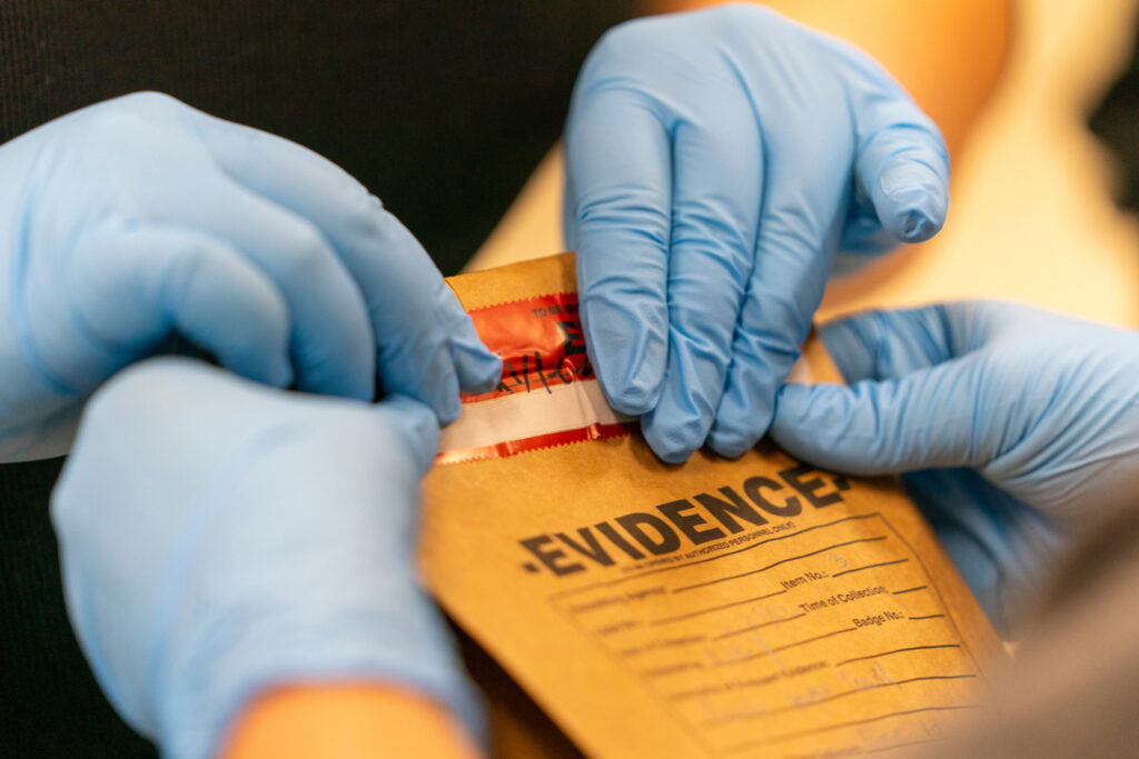 Hands with blue medical gloves close a manilla envelope marked 'EVIDENCE.'