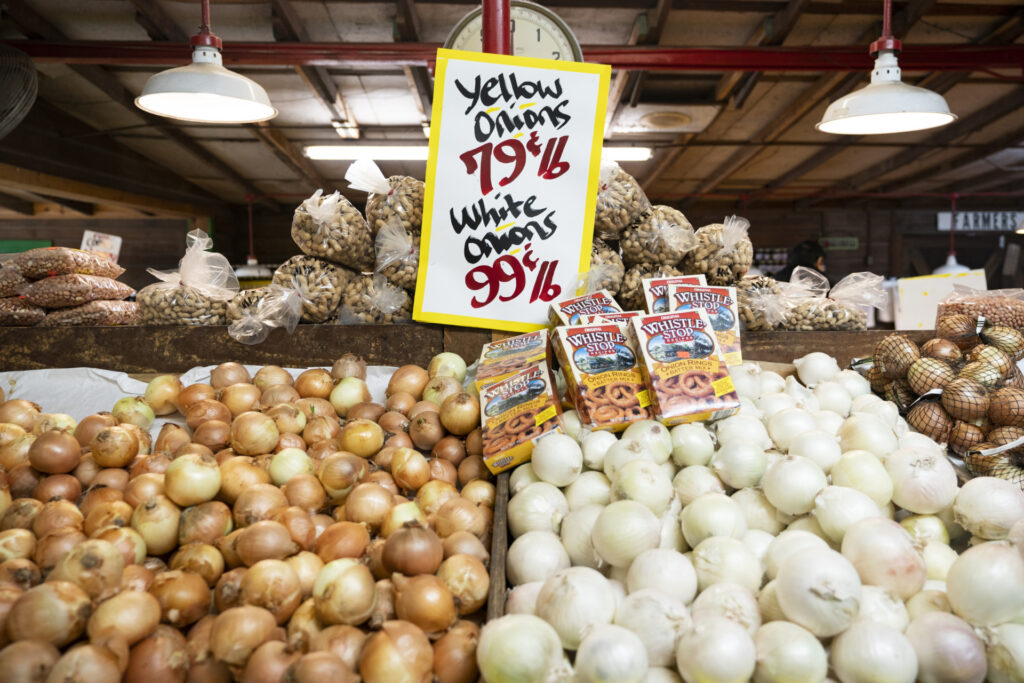 A display of yellow and white onions with a sign that says, "Yellow Onions 79¢lb and White Onions 99¢lb." The fresh market onion industry grew a total of 75,460 tons in 2023. 