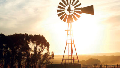 A windmill is in a pasture with a sunny sky in the background.