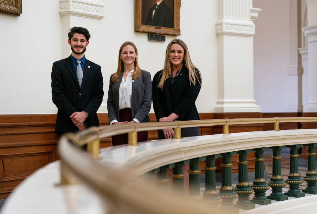 Three college students stand at the rail in the rotunda in Austin at the capital bulding. The young people are part of the agricultural policy internships available to Aggies.