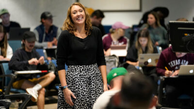 A women smiles in a classroom full of Texas A&M students.