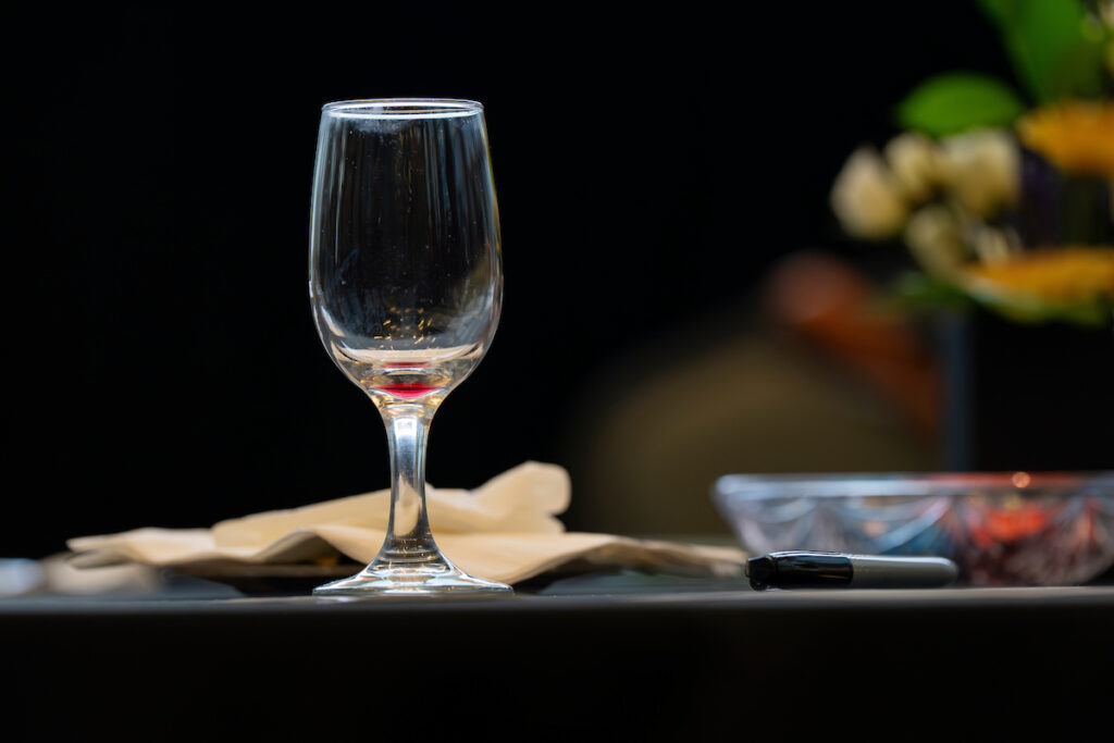 A nearly empty wine glass on a table against a dark background.