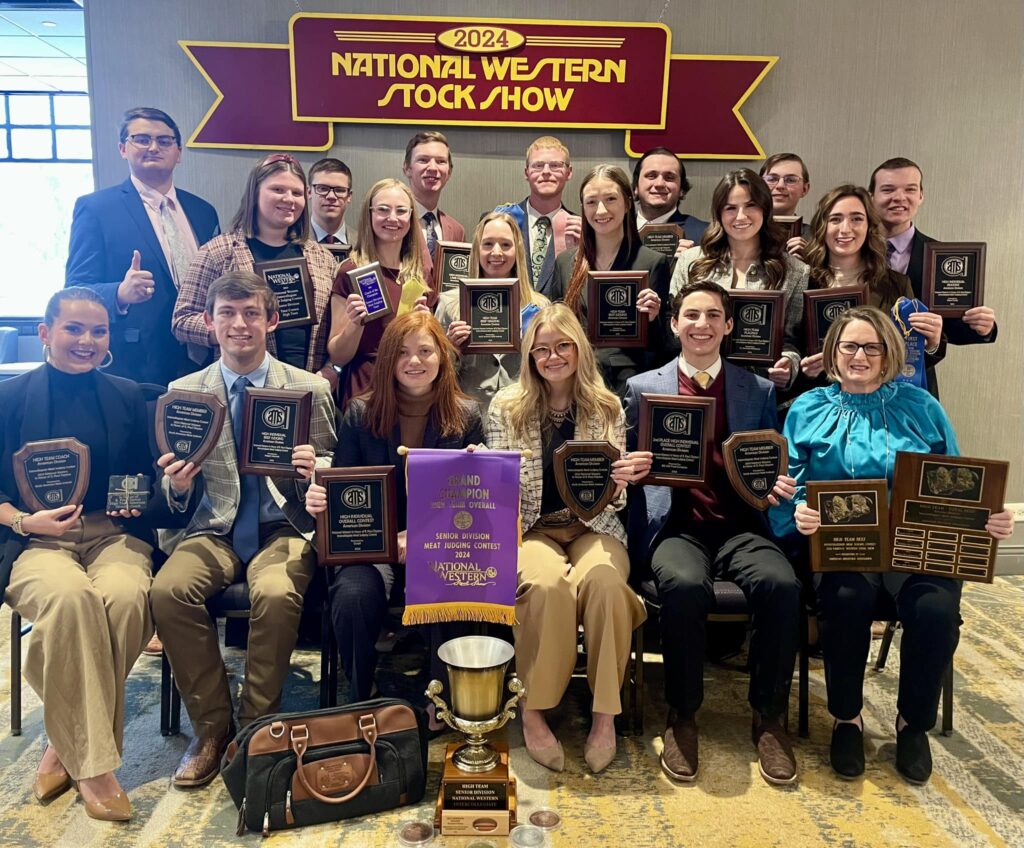A meat judging team photo of many students, male and female holding all kinds of plaques and trophies, showing banners with the main banner reading National Western Stock Show