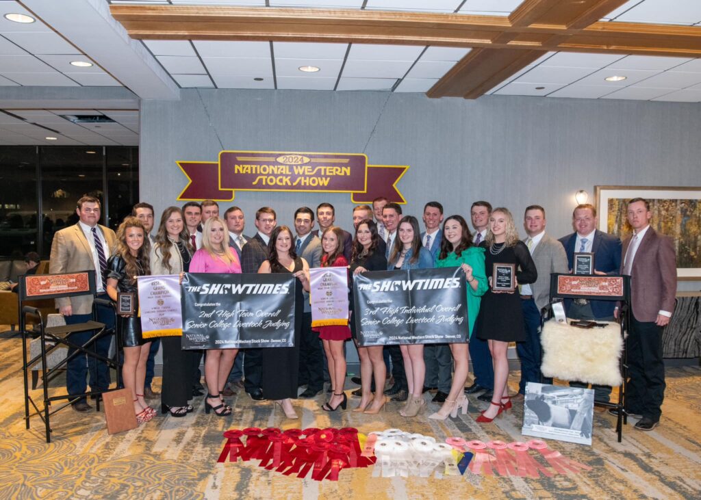 A livestock judging team photo of many students, male and female holding all kinds of plaques and showing ribbons on the floor and multiple larger banners with the main banner reading National Western Stock Show