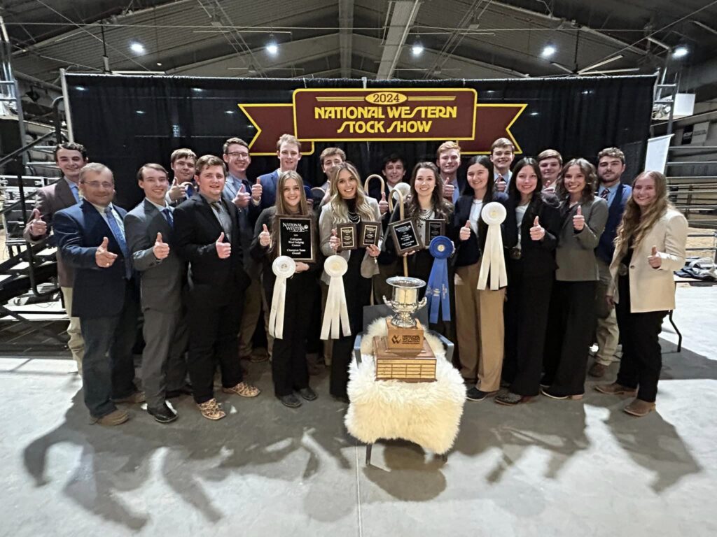 Competitive judging team - the meat judging team photo of many students, male and female, holding all kinds of plaques and ribbons with a larger trophy out front on a wool blanket, with the main banner behind them reading National Western Stock Show