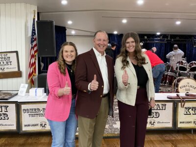 Kaitlyn Kotrla '25 and Delaney Brown '25 stand alongside Chris Skaggs, Ph.D., associate vice chancellor for stakeholder relations and associate dean for student development, at the Brazos County Go Texan Scholarship and Donor Reception. All three are posing with their right thumb up and in front of them. Kotrla wears a pink blazer, black shirt, jeans and boots. Skaggs wears a maroon blazer, white shirt, tan pants and boots. Brown wears a white and tan checkered blazer, black shirt, maroon pants and cream, pointed heels.