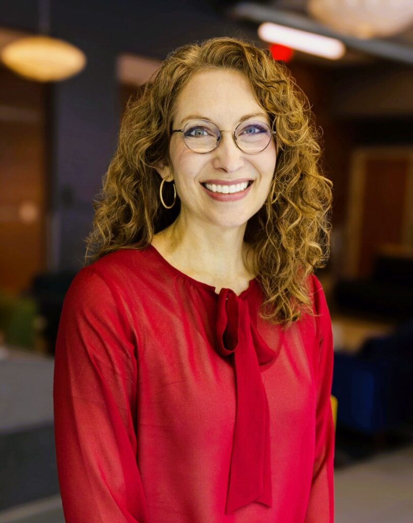 A head and shoulders picture of a woman, food science and technology alum, Janet Adams. She is wearing a red dress and she has curly reddish-brown hair and she is wearing glasses. 