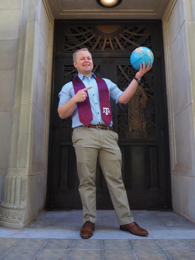 A man standing outside in front of a door with a globe on his hand, Luke Drosche