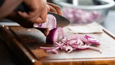 A person is cutting an onion to be cooked in a dish.