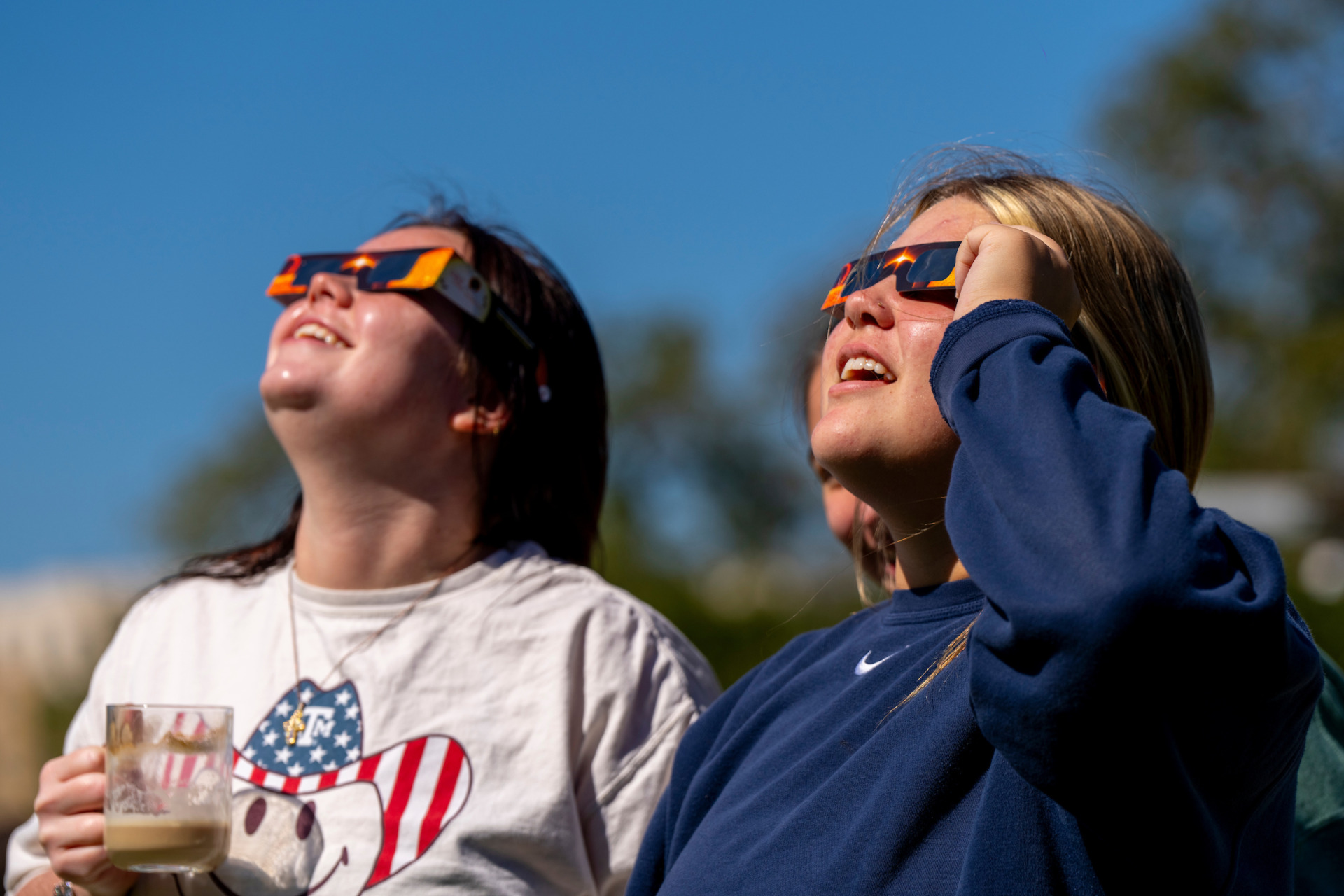 Two female students with eclipse-viewing glasses look toward the sun during an eclipse in 2023. 