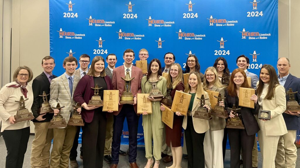 group of students and coaches holding banners, trophies, plaques and ribbons in front of a 2024 Houston Livestock Show and Rodeo backdrop