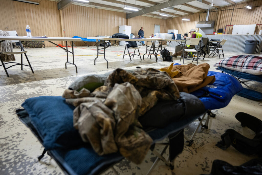 several cots can be seen with sleeping bags in front and tables with equipment and people working in the background as AgriLife Extension provides wildfire disaster response