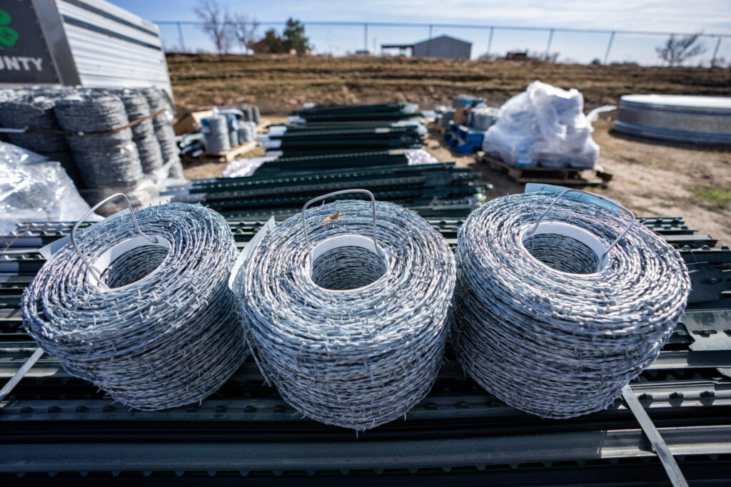 rolls of barbed wire are collected at an Animal Supply Point along with other fencing supplies in the background.