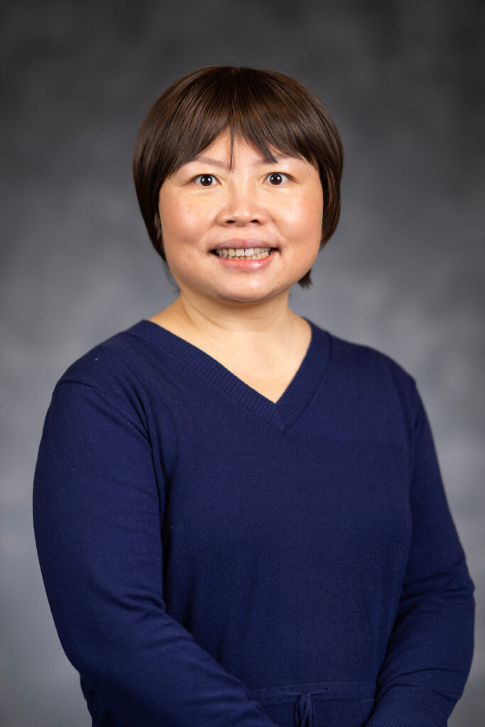 Dr. Zhihong Xu wears a navy sweater against a gray background in orofessional headshot.