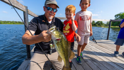 A man holds a large bass as two little boys look on.