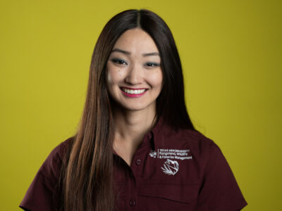 A headshot of a young woman with long dark hair wearing a maroon shirt agaisnt a chartreuse background