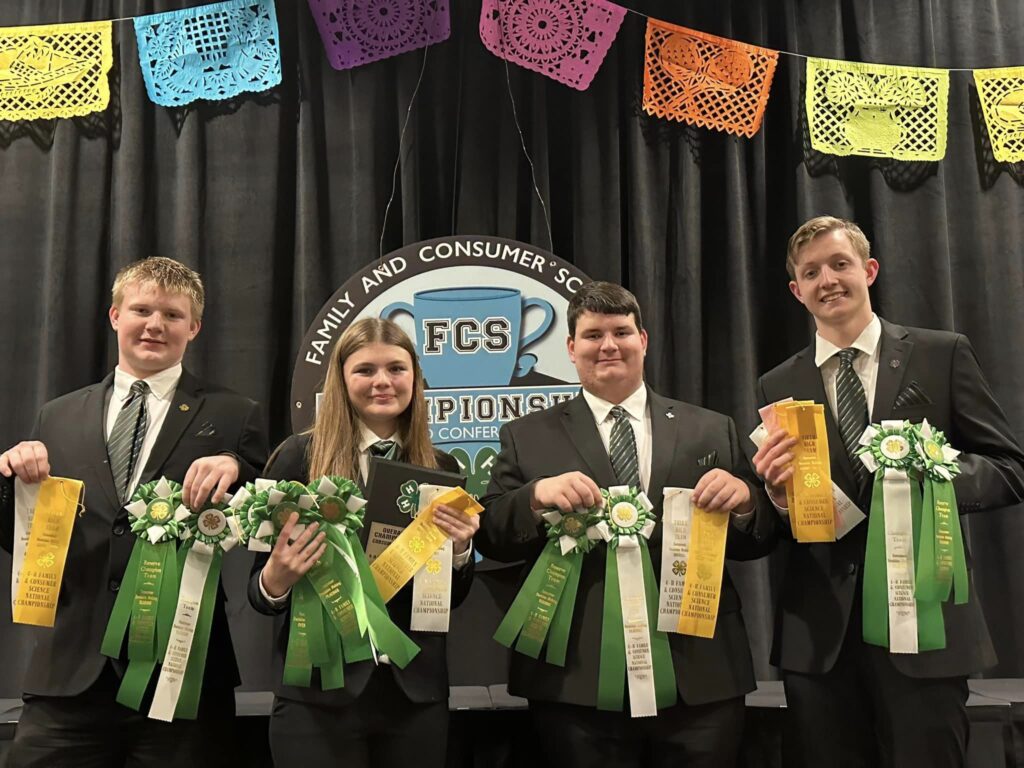 A young woman and three young me pose while holding the ribbons they won at the National 4-H Consumer Decision-making contest.