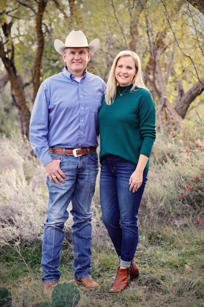 a man in a cowboy hat and jeans and a woman in a green sweater stand in a fall outdoor setting - Casey and Cara Bradshaw