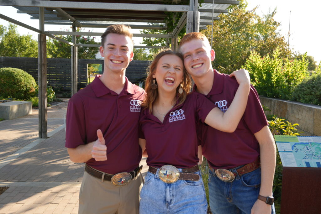 Three people in maroon polo shirts stand close together, while one person holds his thumb up.