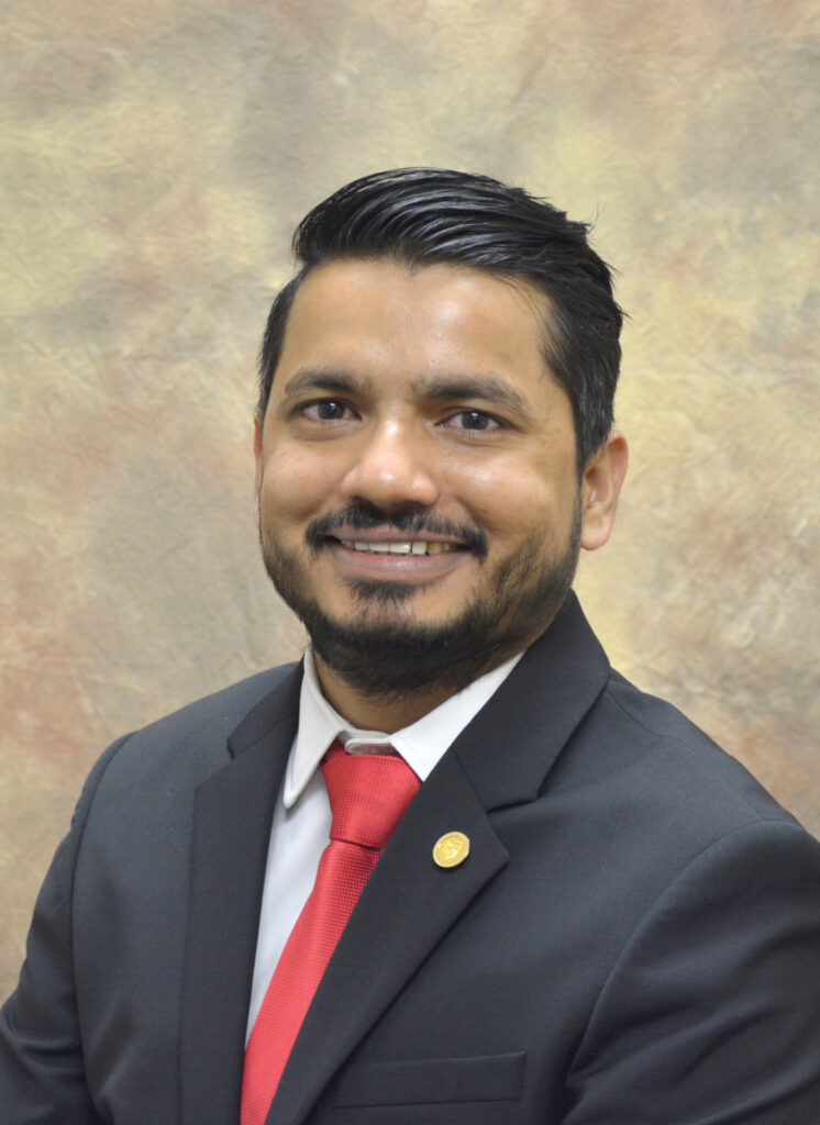 a headshot of a man, Kiran Gadhave. He is wearing a white shirt, red tie and blue sport coat