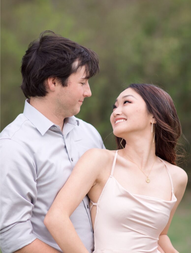 An engagement photo in which a young couple stare into each other's eyes. Both have dark hair and wear light-colored formal wear. Hannah Evans and Lucas Stevens met while at Texas A&M.