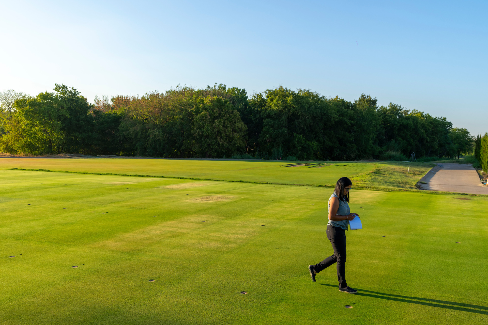 A woman walks across a golf green. 
