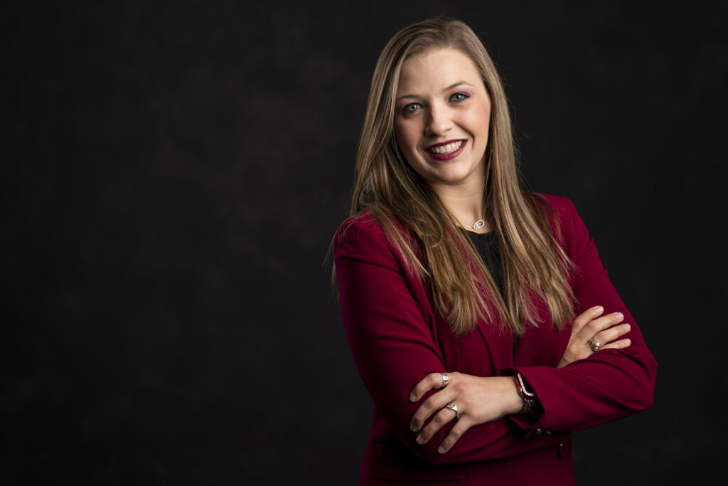 Carissa Beamon stands with her arms crossed while wearing a maroon blazer and black shirt. She is an advisor for several majors in the College of Agriculture and Life Sciences and oversees a team of 11 advisors in the Kleberg Advising Hub. 