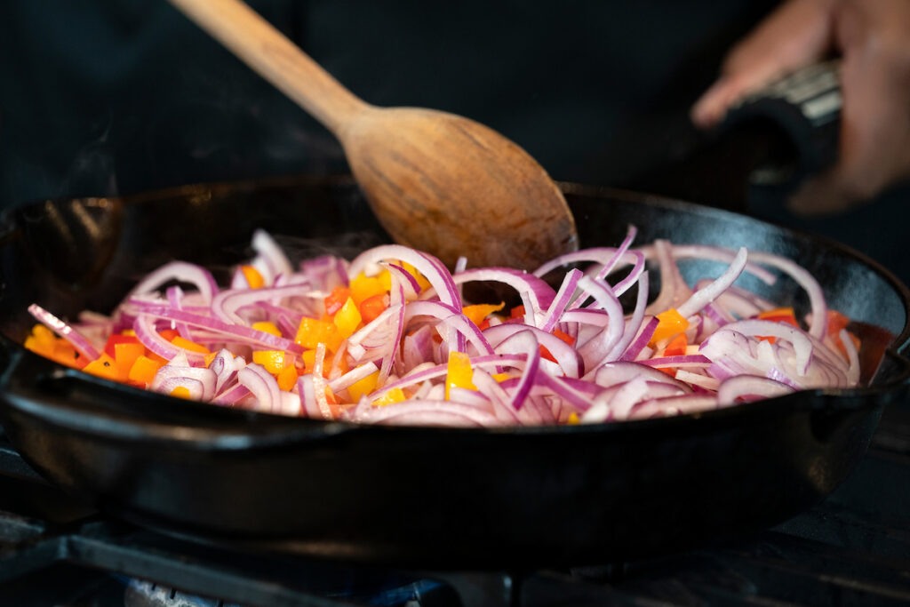 A person is cooking a dish with onions and bell peppers. Participants of the "Cooking with Cultures" class will learn how to cook healthy dishes from four different countries.