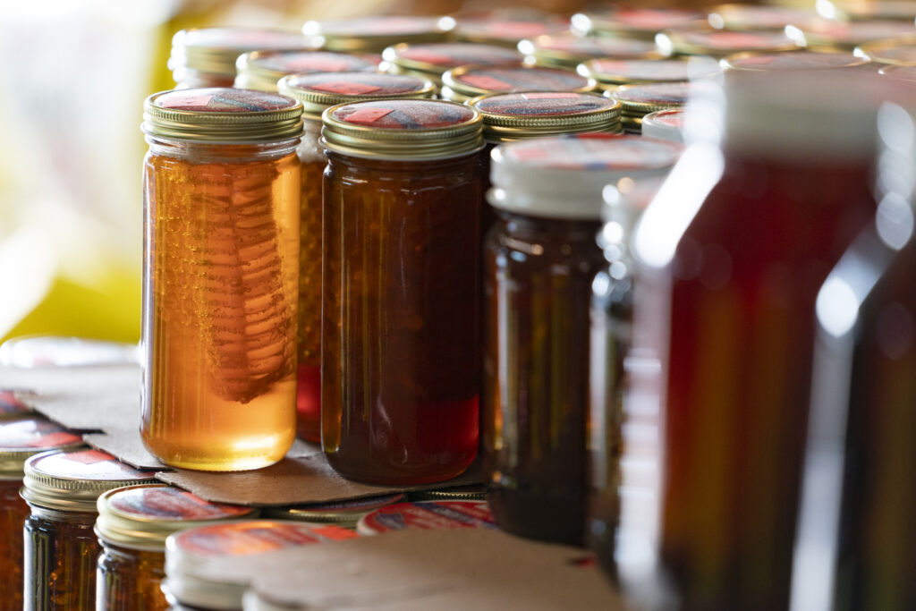 Tall jars of honey in various hues of amber at a farmers market.