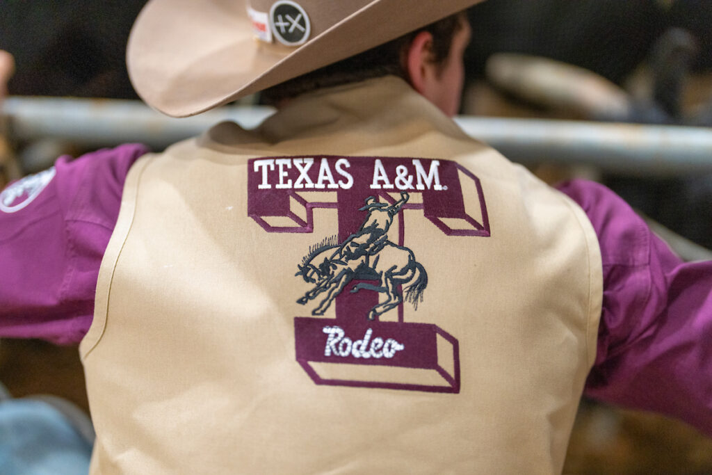 The back of a rodeo vest that has the large block letter T with Texas A&M Rodeo written inside it and a cowboy riding a bucking horse across the center of the T