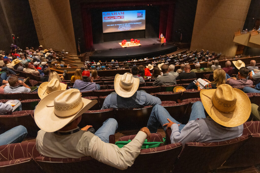 looking down in a large auditorium at a presenter at the Beef Cattle Short Course, many cowboy hats throughout the crowd.