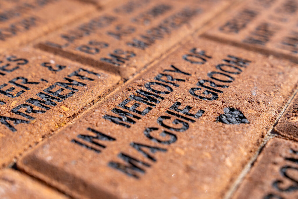 A closeup of an engraved bricks, the closest reads In Memory of Maggie Groom