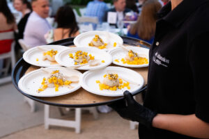 A person serves a platter of food to attendees at an event.