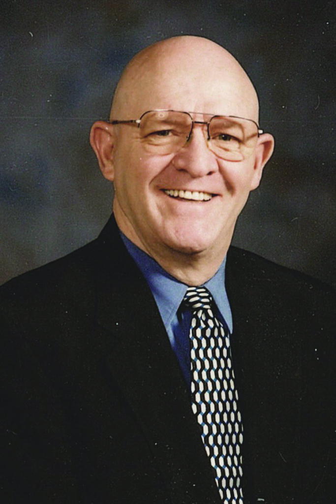 Headshot of Gary Smith. He has on glasses and is wearing a blue shirt with a dark and tan patterned tie and a dark colored jacket.