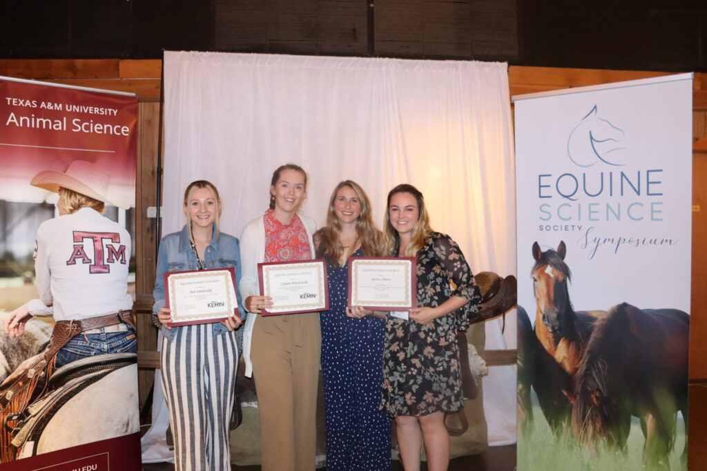 Four women stand holding certificates between two banners, one from Texas A&M University Animal Science and the other from Equine Science Society