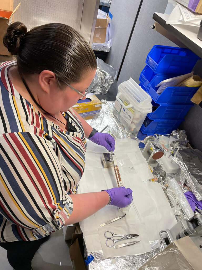 lady in striped shirt works with gloved hands to set up a soil sample in a lab setting