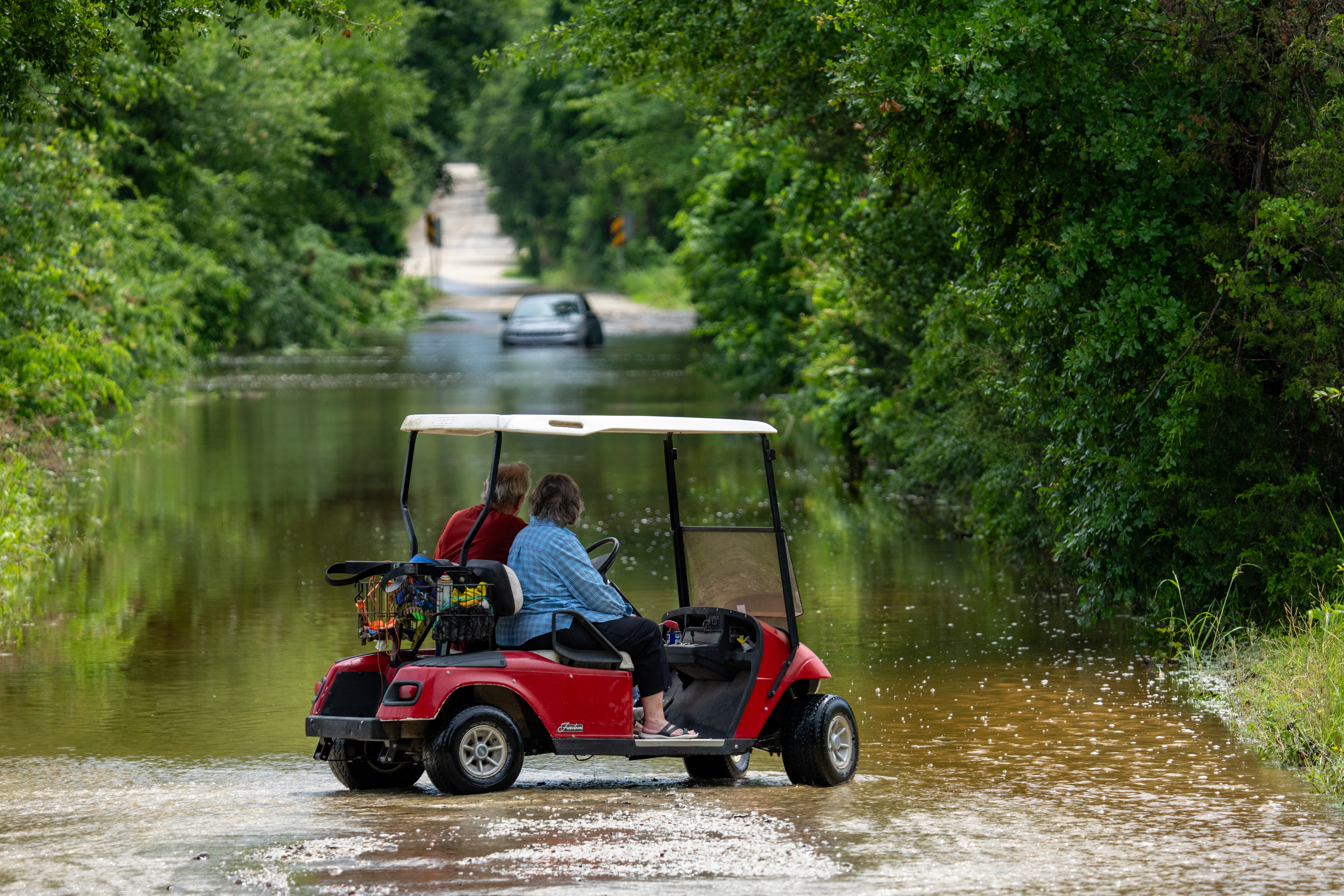 Car in flooded waters as people on golf cart look on.