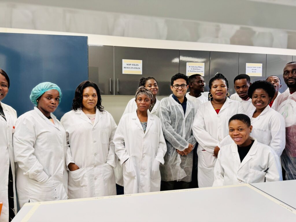 A group of researchers and lab technicians in white lab coats smiling in their malaria research lab in Equatorial Guinea