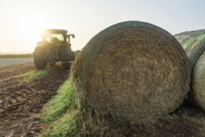 a bale of hay in the foreground with a green tractor in the background