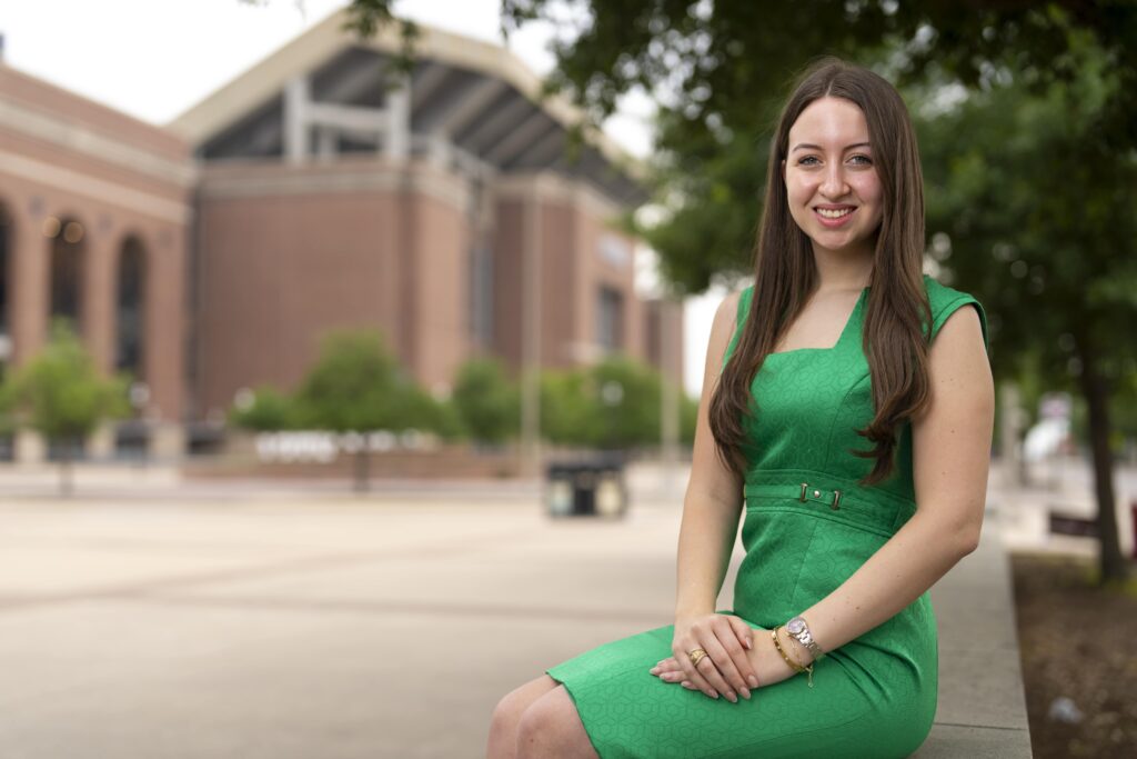 A woman in a green dress sits in front of the Texas A&M University football field. Jade Williams '24 has taken advantage of the opportunities in Aggieland.
