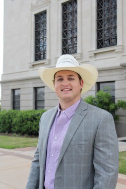 A smiling male student in a suit jacket outside with a cowboy hat on