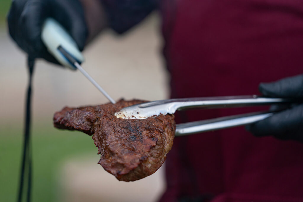A grilled steak held in a set of tongs with a thermometer stuck inside