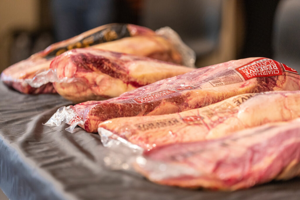 Several cuts of meat covered in plastic wrap, sitting on a black table. 