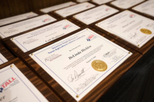 A row of graduation plaques for the AgriLife Extension TALL program. They are mounted on wood and feature a gold seal.