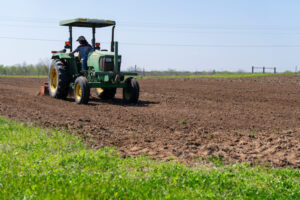 A person is tilling soil with a tractor at a farm in Corpus Christi.