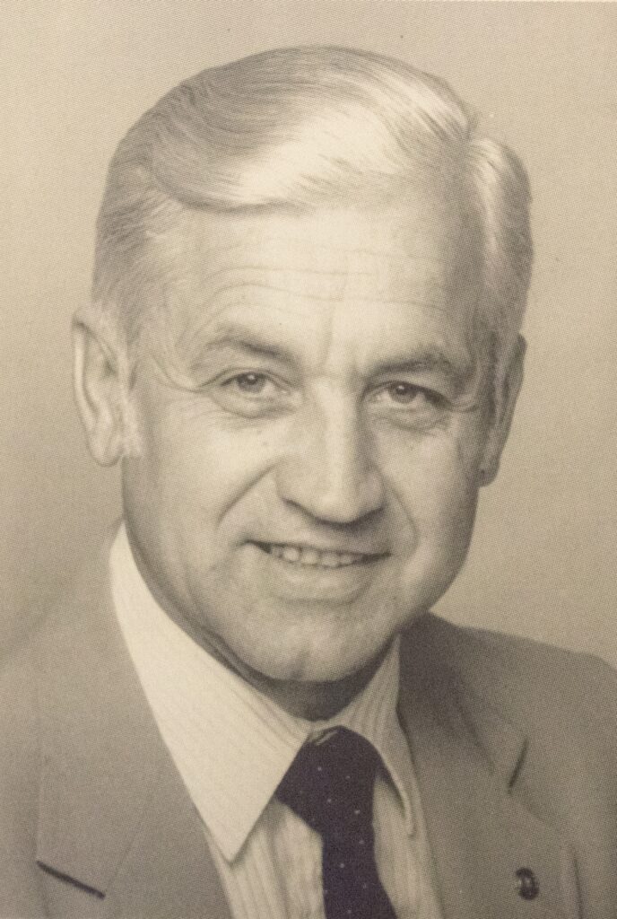 a black and white photo of a man, Konrad Eugster, with white hair in a suit and tie.