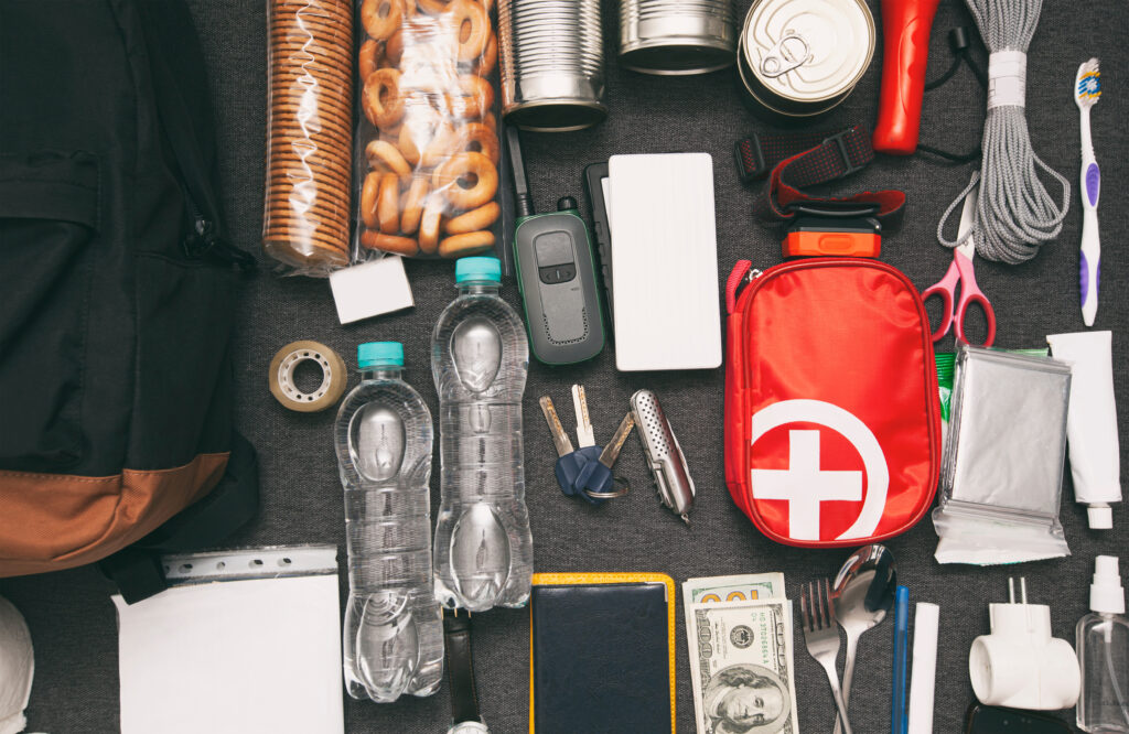 An assortment of emergency supplies like scissors, tooth brush, rope, keys, food, first aid kit, money, weather radio, flashlight and other things for a hurricane go bag.