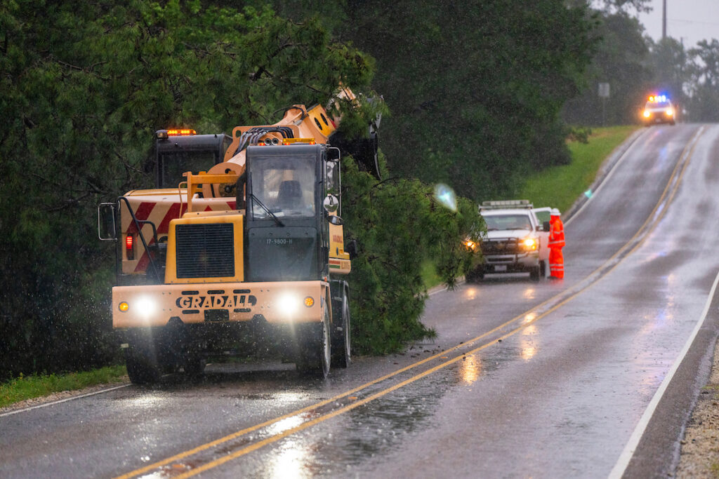 Emergency vehicles for tree removal on road made wet from rain and flooding due to Hurricane Beryl. 