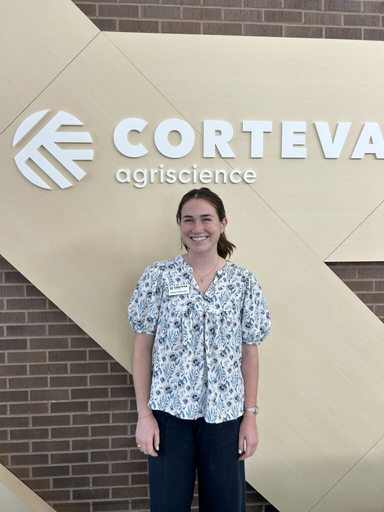 A woman stands in a floral shirt in front of a Corteva Agriscience building sign. 